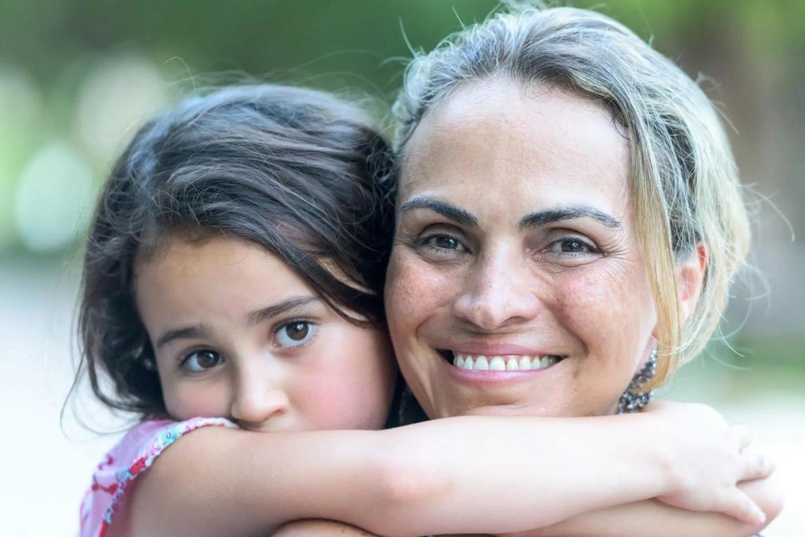 Smiling hispanic mature woman posing embracing her six years old daughter