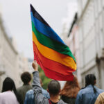 The pride flag held up in a group of people who look to be marching down a street.