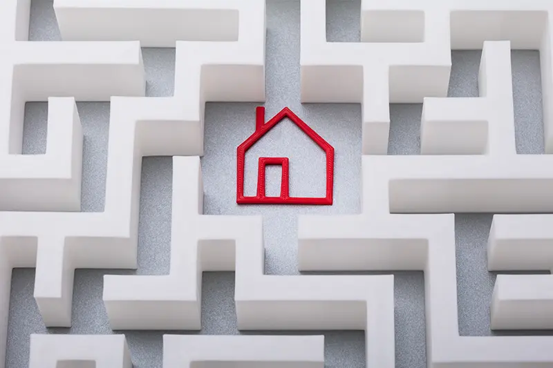 The outline of a home made with red yard in the middle of a maze with white walls and a gray floor.