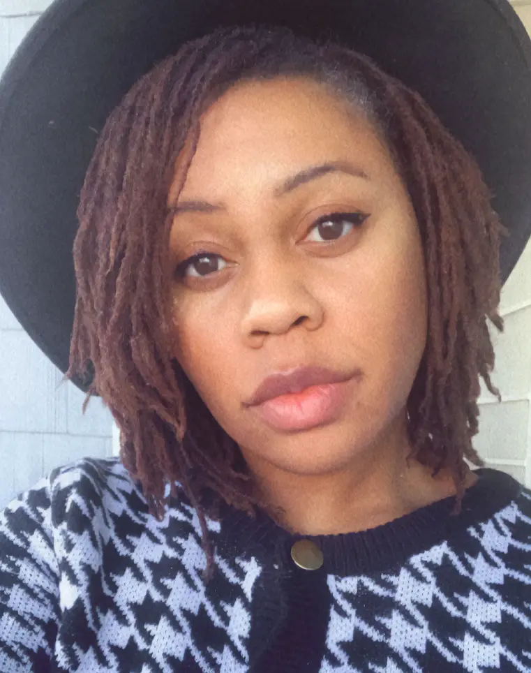 A female presenting individual with a black hat and white and black sweater looking with intent towards the camera.