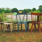 A field with a table and multicolored chairs placed around it.