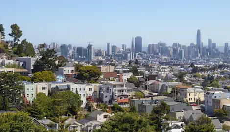 The San Francisco Skyline looking north from the south of the city with houses on a hill lined with green trees.