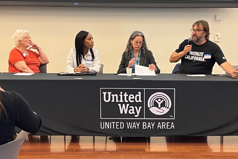 Four individuals seated at a table with a black tablecloth and the United Way Bay Area logo in white.