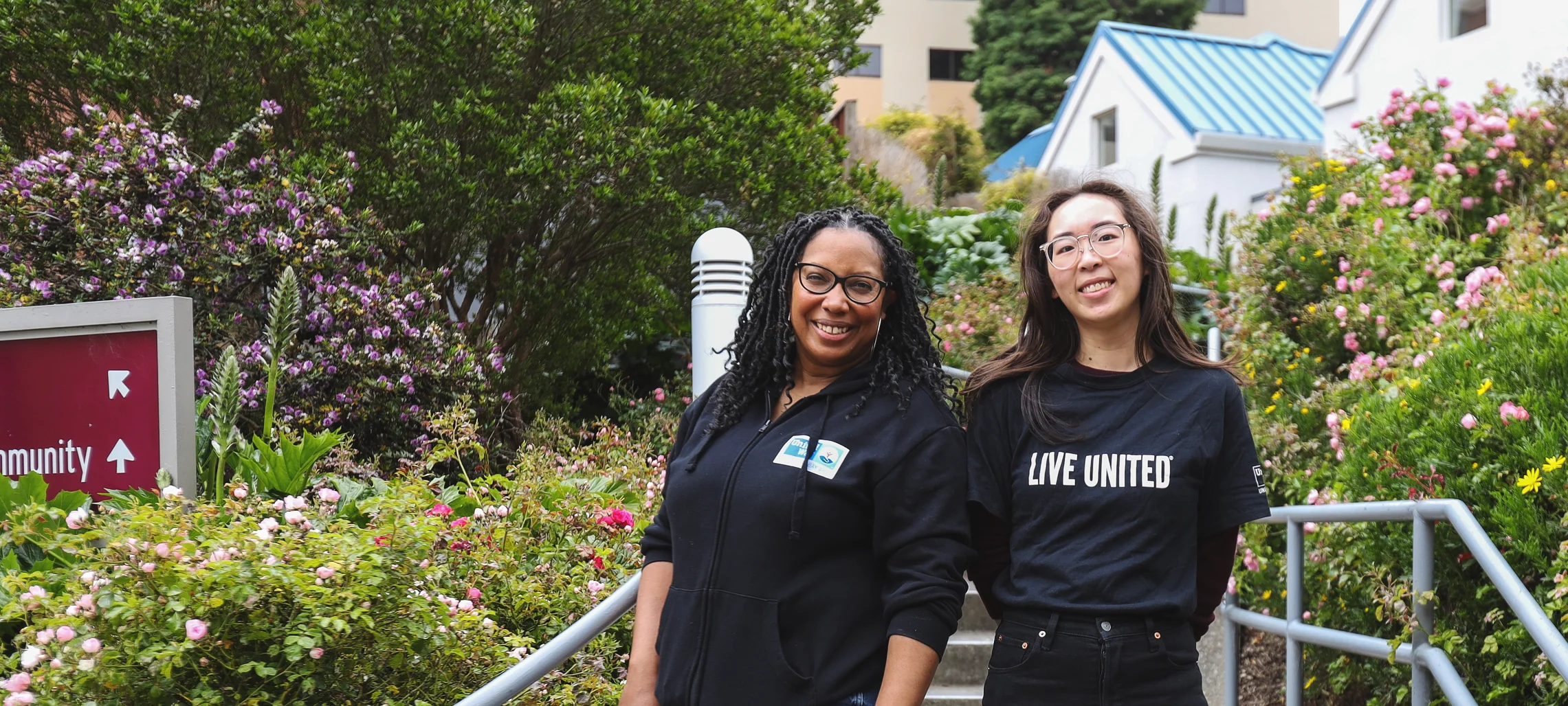 Two young female presenting individuals wearing black shirts with United Way Bay Area branding smiling at the camera.