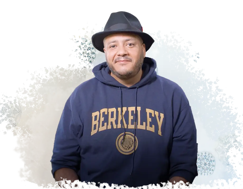 A male presenting individual with a fedora and a navy blue sweatshirt with the word 'Berkeley' on it and the University of California, Berkeley's logo.