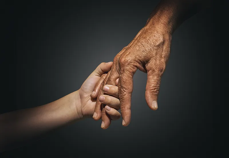 The hands of two individuals held together against a dark background.