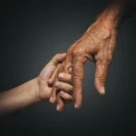 The hands of two individuals held together against a dark background.