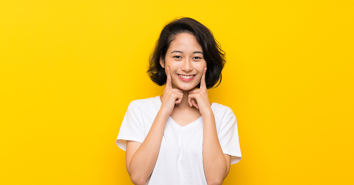 A female presenting individual against an yellow-orange background with a big smile