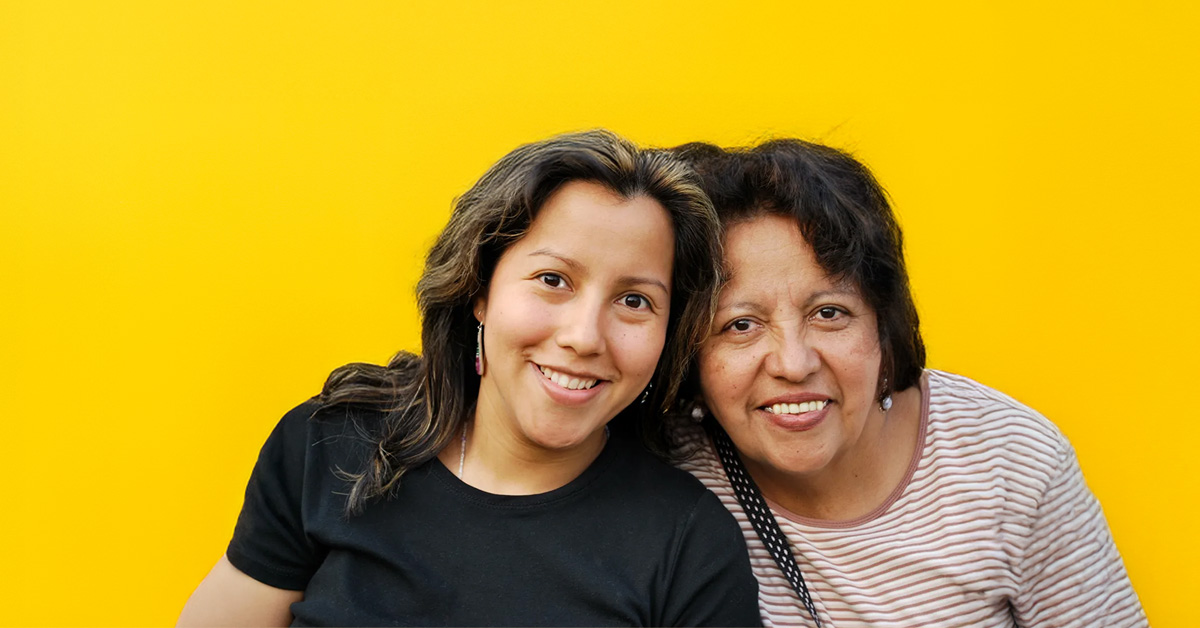 two female presenting individual against a yellow-orange background with a big smile