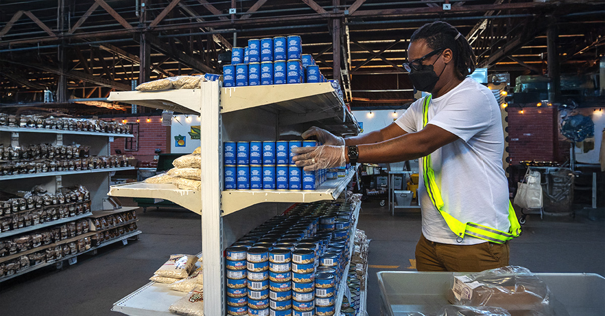 A male presenting individual stacking cans at what looks to be a food processing center for emergencies.