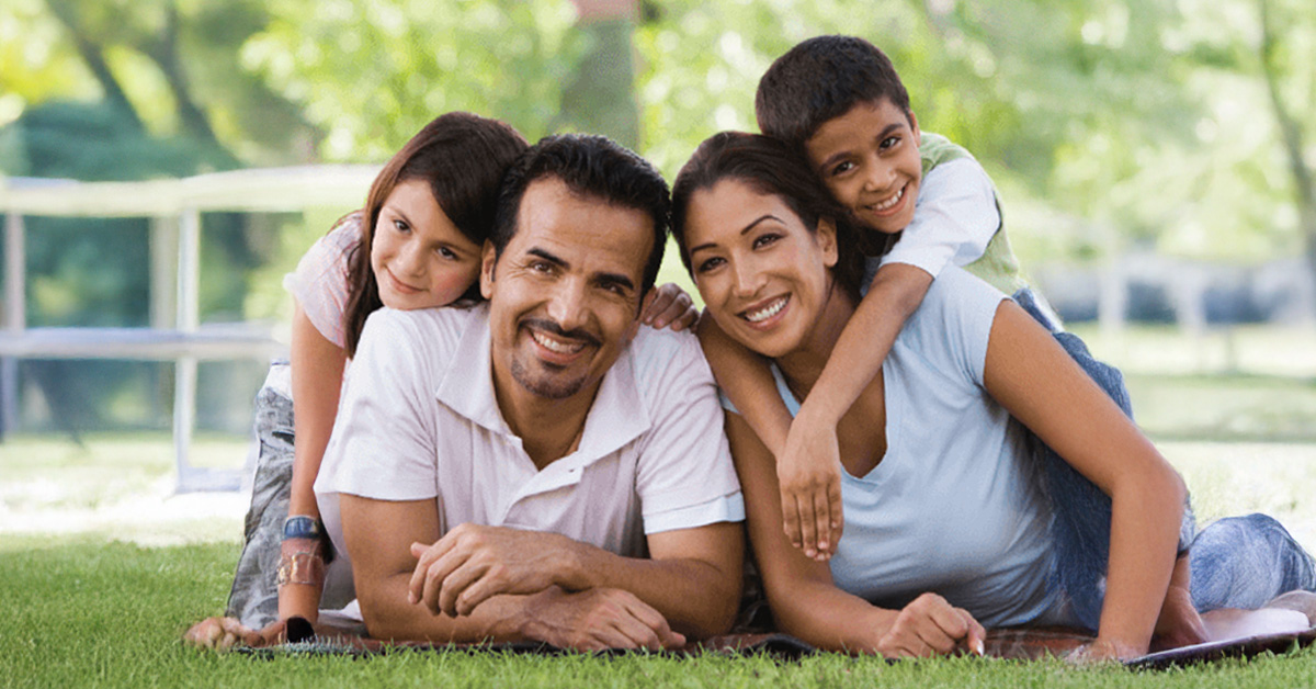 A family consisting of two adults and two children on a green lawn.