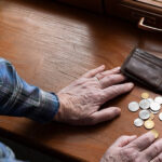 An older individuals hands on a table with wallet open and change out.