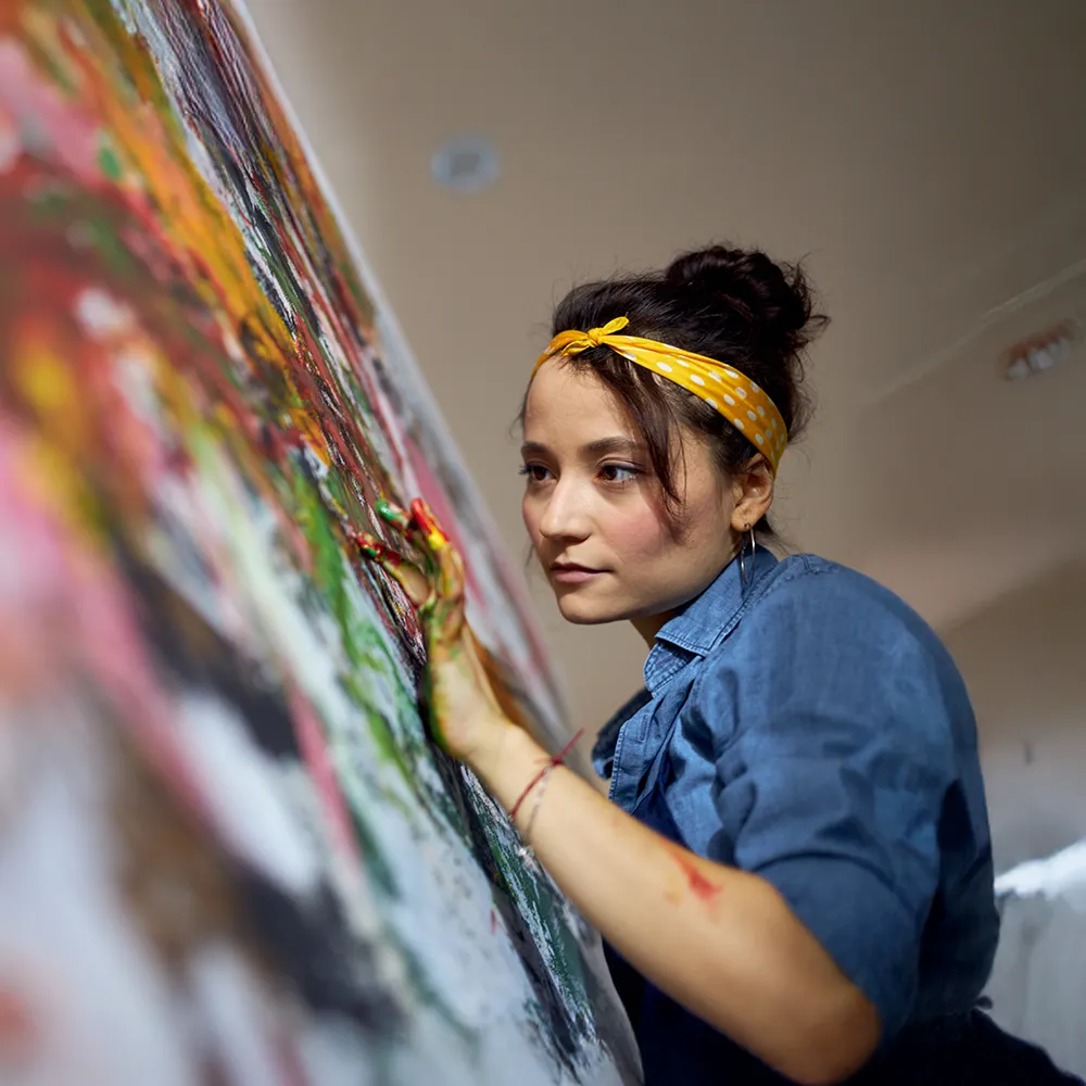 An individual with paint on their hands using them to create art on a canvas.