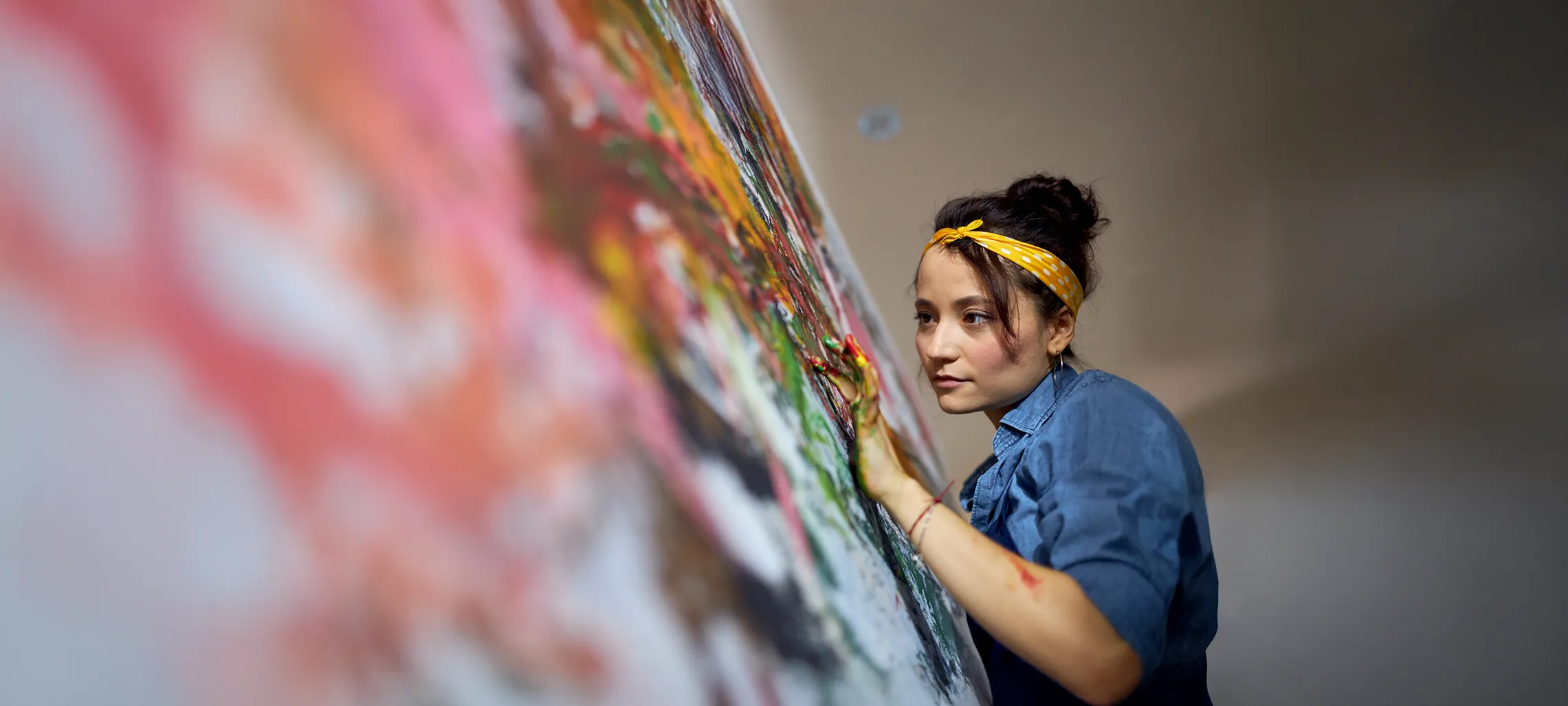 An individual with paint on their hands using them to create art on a canvas.