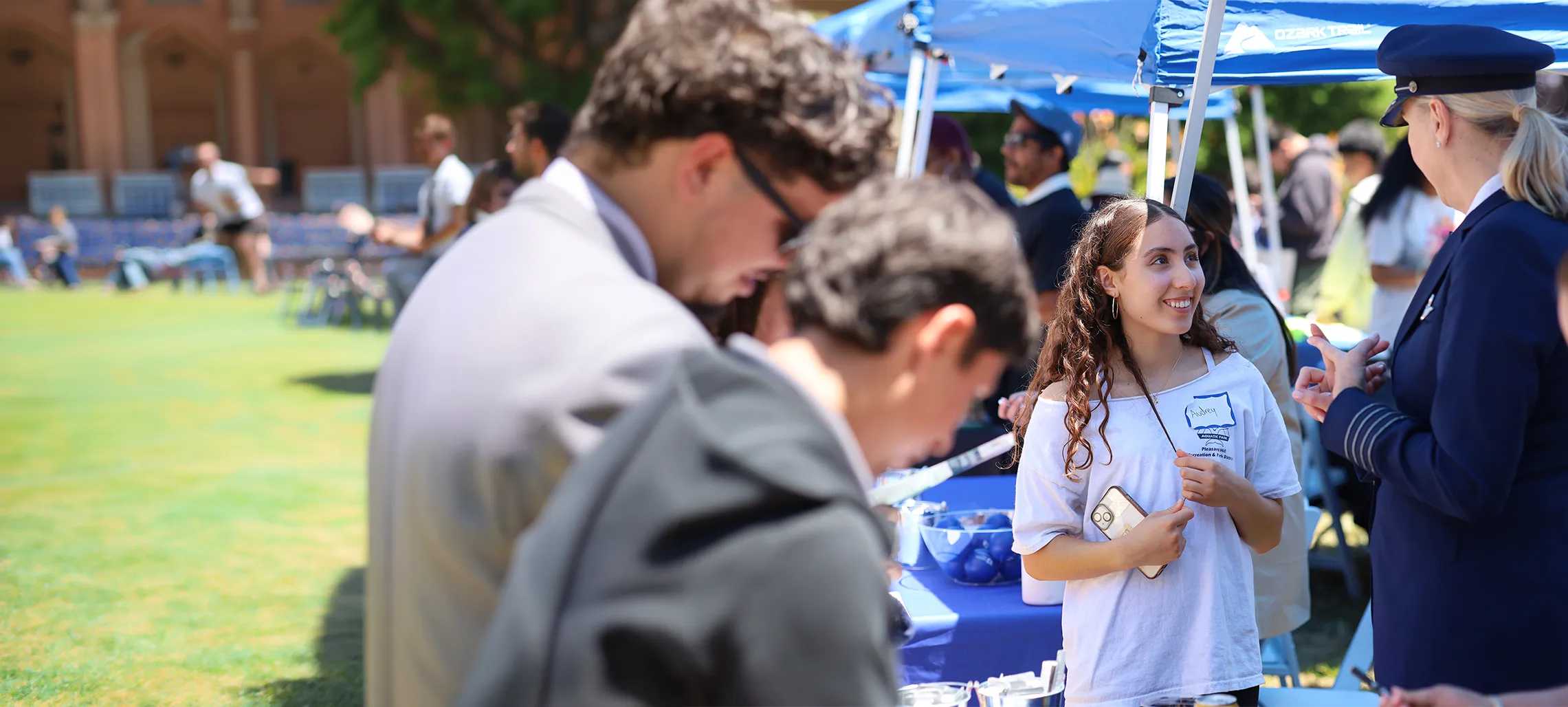 A female presenting individual amongst a group of people speaking with an individual who appears to be in a formal military outfit.