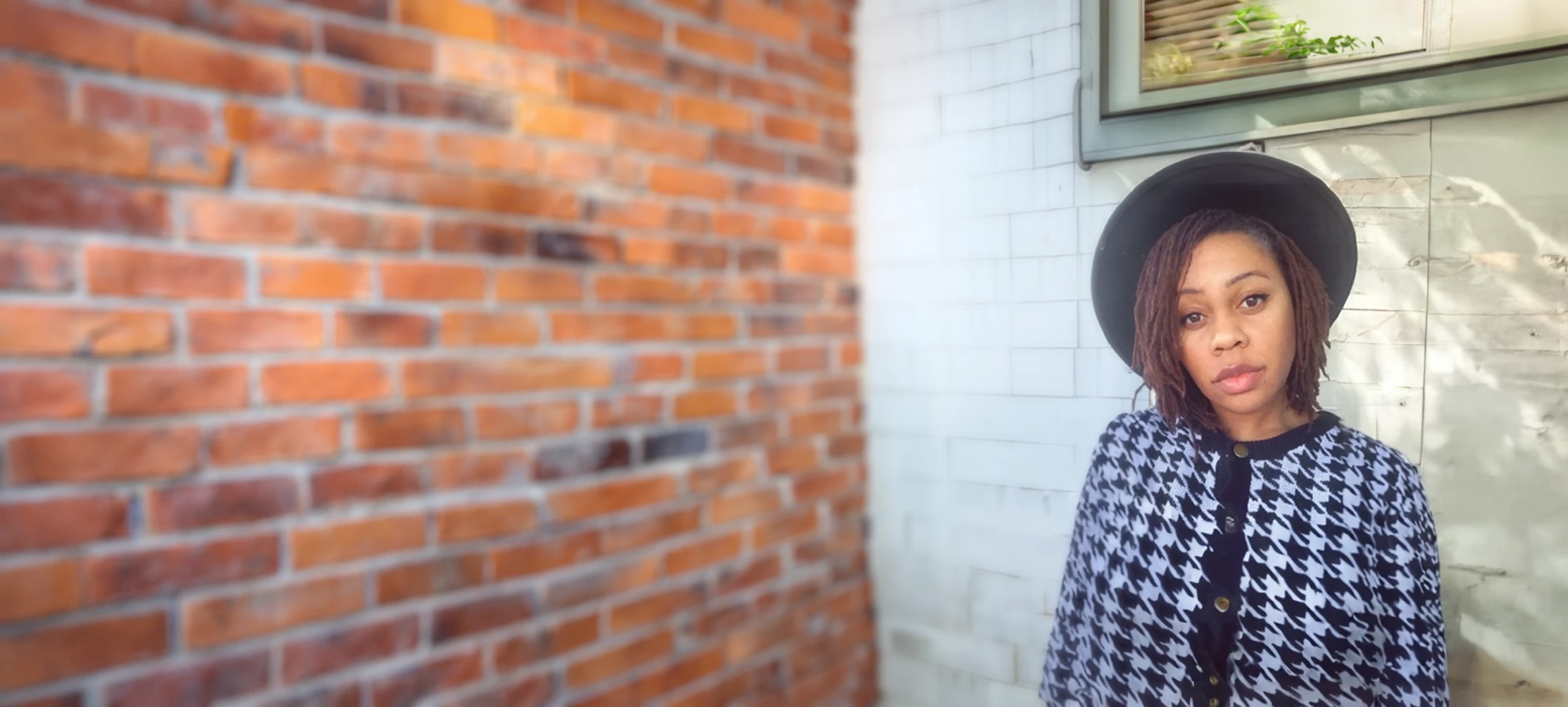 A female presenting individual against a white brick wall.
